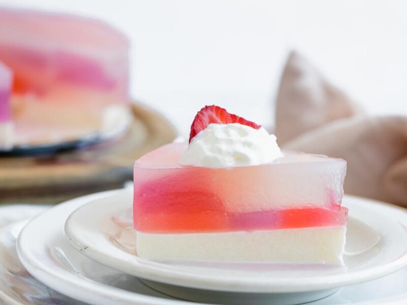 Strawberry-topped stained glass cake slice on a white plate with more slices in the background.