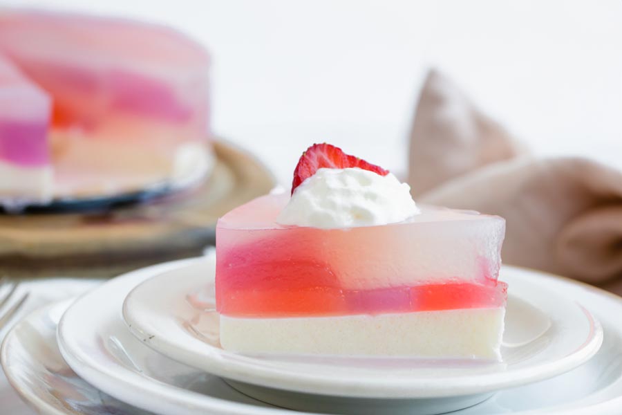 Strawberry-topped stained glass cake slice on a white plate with more slices in the background.