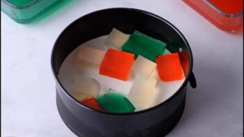 Cubes of red, green, and clear gelatin scattered on top of the set white layer in the pan.