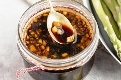 a spoon coming out of a small jar containing stir fry sauce with minced garlic