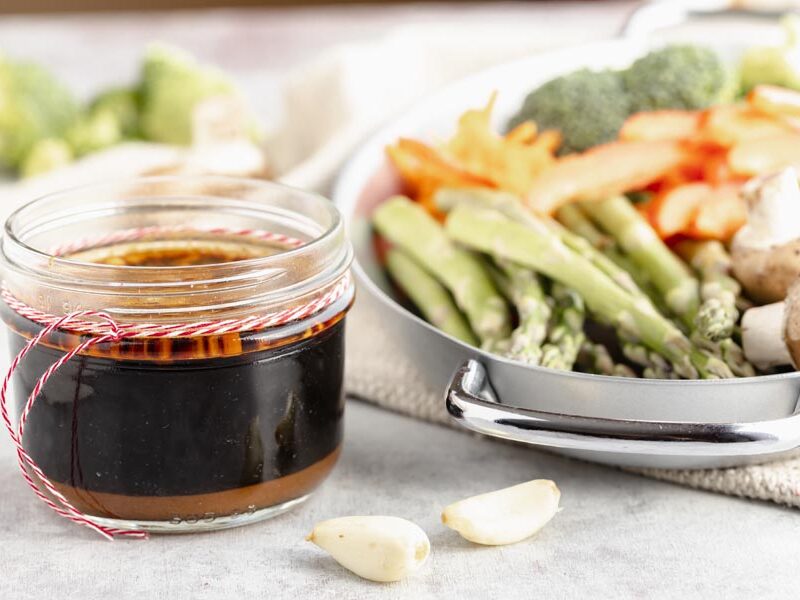 Jar of homemade stir-fry sauce beside raw asparagus, mushrooms and garlic.