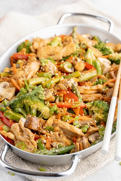 a skillet with cooked stir fry with chicken, broccoli, red bell pepper and topped with sesame seeds