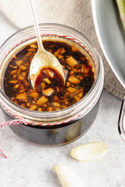 a spoon lifting up a spoonful of sauce with mined garlic from a mason jar