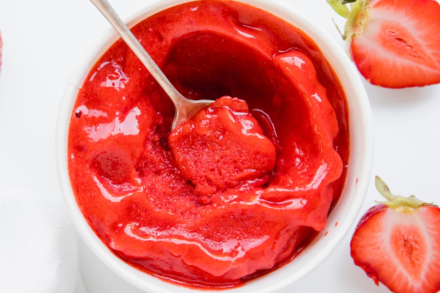 top down view of a white container with sorbet inside with sliced strawberries near