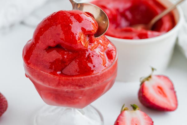 scooping red strawberry sorbet with a spoon with sliced strawberries near