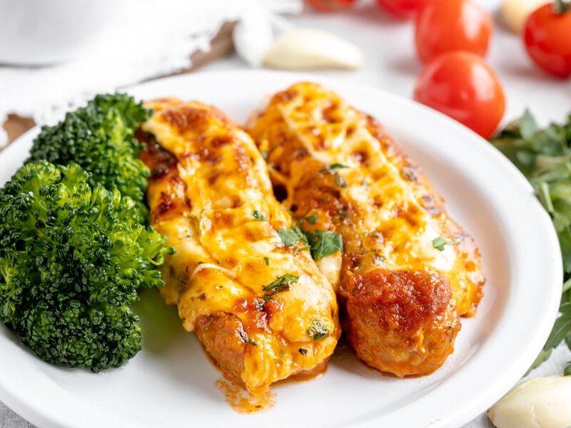 two stuffed sausages on a plate with a side of broccoli