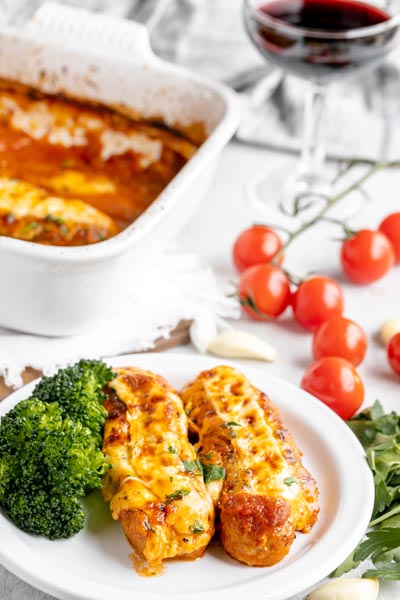 dinner table with a glass of wine behind a plate with two cheese stuffed sausages and broccoli on a plate