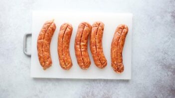 five sausages on a white cutting board with a vertical slit down the center of each sausage