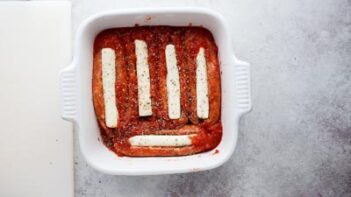 a white casserole dish with stuffed sausages mixed with marinara sauce and topped with italian seasoning