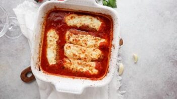 melted cheese tops sausages with pasta sauce in a baking dish