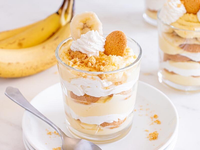 A sugar free banana pudding in a glass dish on top of plates with real bananas in the background.