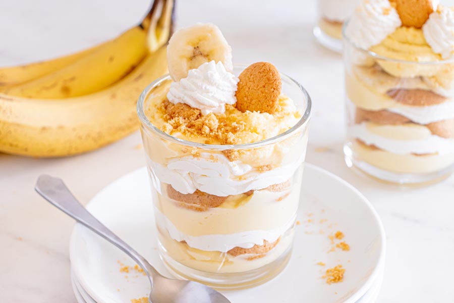 A sugar free banana pudding in a glass dish on top of plates with real bananas in the background.