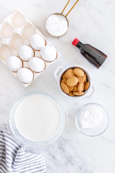 Ingredients to make banana pudding grouped together -eggs, cream, sweetener, wafers and flavoring.