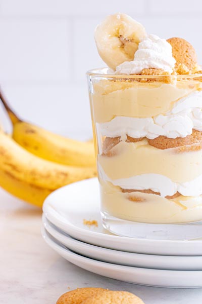 A close up of a layered banana pudding with different levels of yellow pudding, whipped cream and cookies.