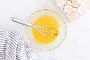 Egg yolks in a glass bowl with a whisk in the center.
