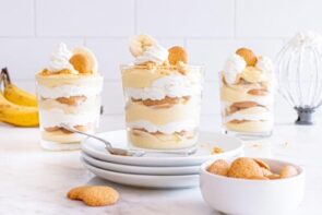 Finished banana pudding trifles with one stacked on three plates and a bowl of vanilla wafers in front.