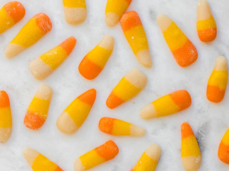 Orange, yellow and white sugar-free candy corn scattered on a marble surface.
