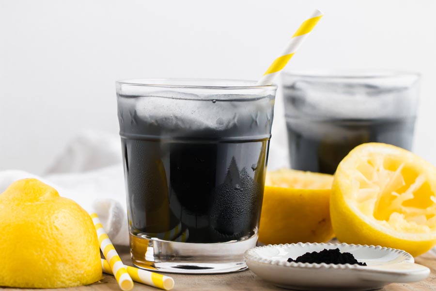 close up of charcoal lemonade with a straw and lemons