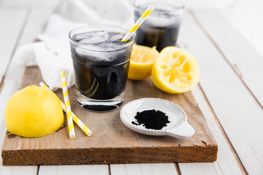 two glasses of detoxifying lemonade with powdered charcoal in a small dish next to it