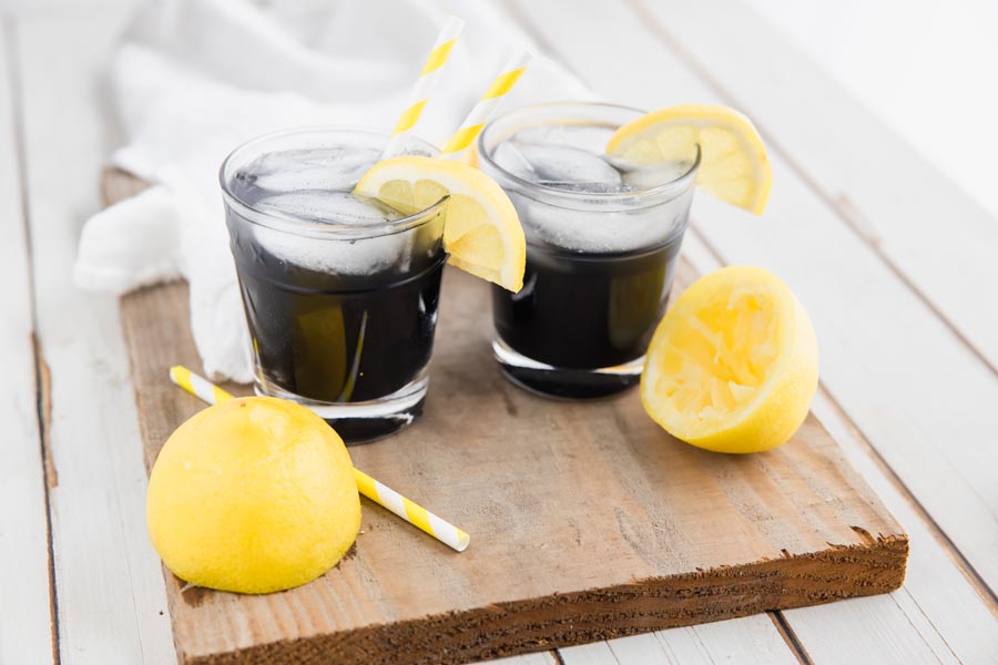 two glasses of black lemonade on a wooden board with lemons