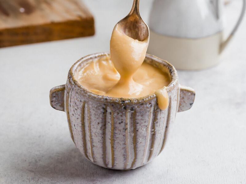 A spoon dipped into the sweetened condensed milk and pulls out to show it dripping off the spoon.