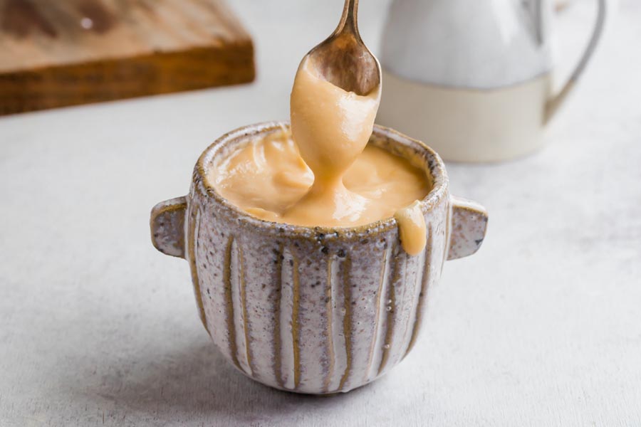 A spoon dipped into the sweetened condensed milk and pulls out to show it dripping off the spoon.