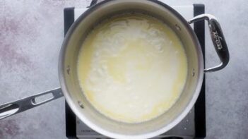 A saucepan filled with cream and butter boiling over a stovetop burner.