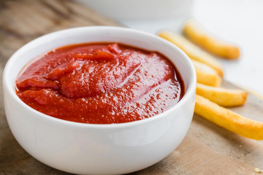 a bowl filled with glossy red ketchup and a couple of french fries next to it