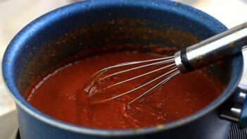 a wire whisk laying in a saucepan of tomato paste sauce