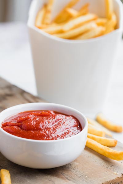 a bowl of ketchup next to fries with a white carton of keto fries in the back ground