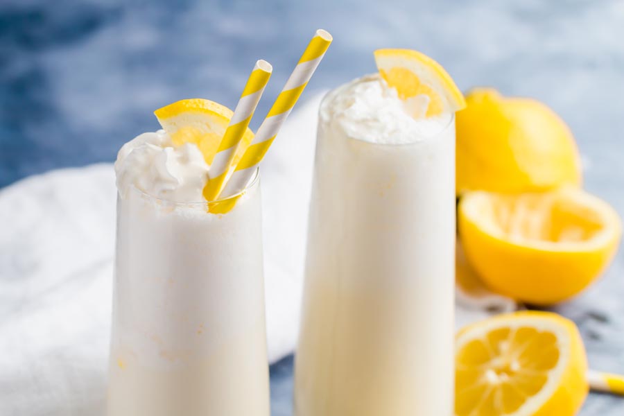 two glasses of keto frozen lemonade on a blue background with striped yellow straws