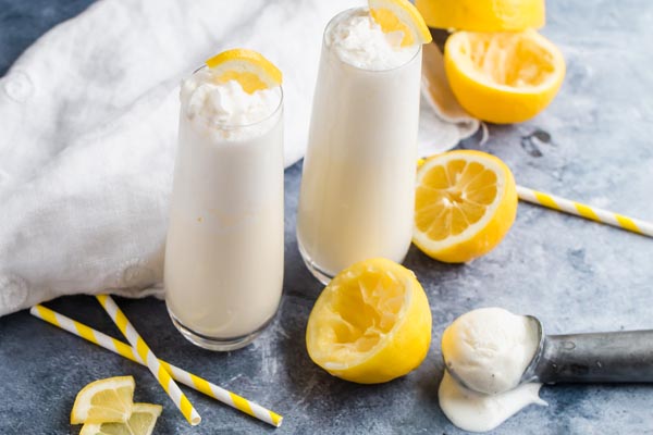 two milkshake glasses with frozen lemonade, straws and lemons scattered around