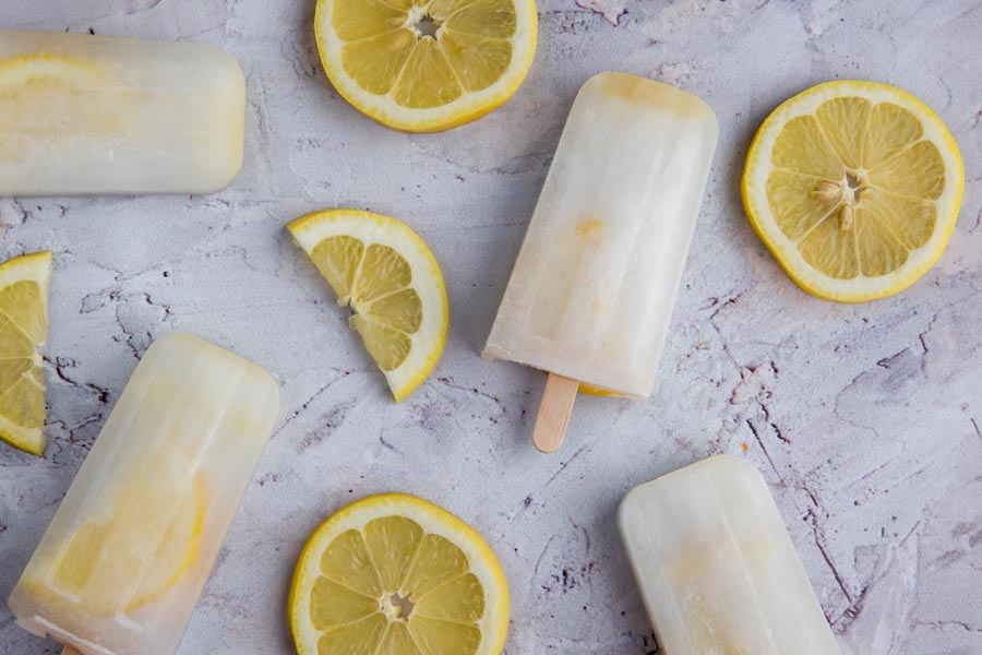 keto lemonade popsicles scattered on a counter with sliced lemons around