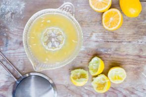 A juicer with fresh lemon juice inside surrounded by lemons