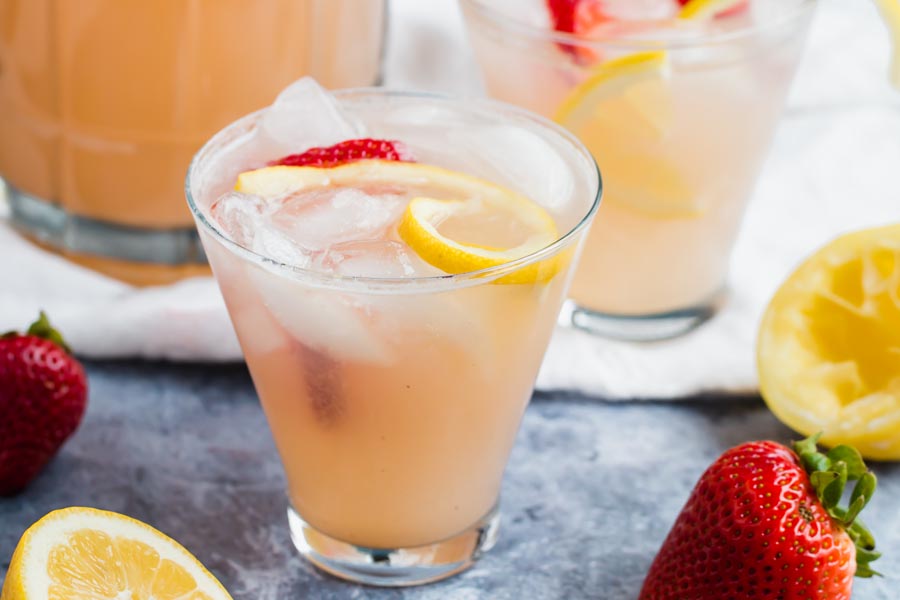 chilled glass with pink strawberry lemonade and a lemon peel inside