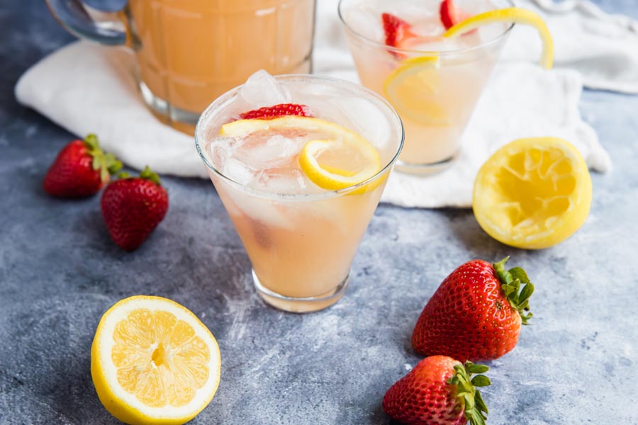 two glasses of sugar free lemonade with strawberries and lemons nearby