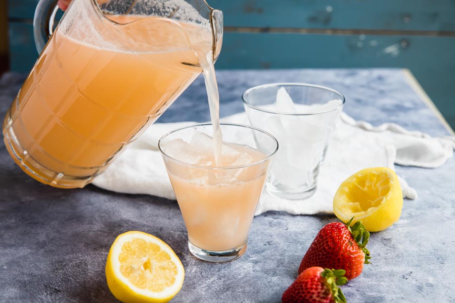 pour a glass of strawberry lemonade form a clear pitcher