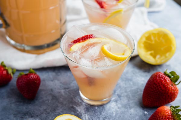 a glass of pink lemonade with a lemon slice and strawberries near by