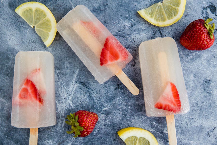 three strawberry lemonade pops on a marbled backdrop with sliced lemons and strawberries