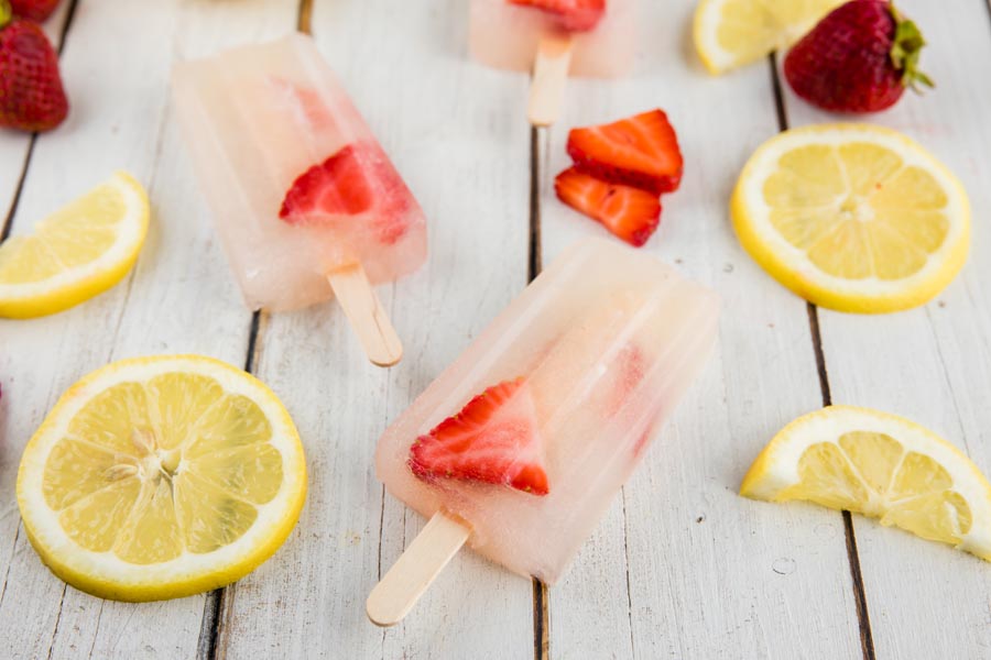 angled shot of popsicles scattered on a wooden counter with whole lemon slices