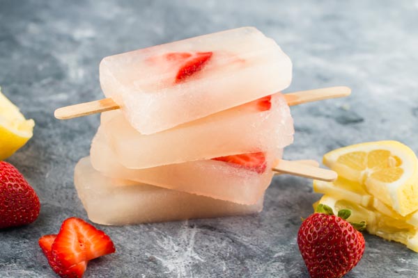 four strawberry lemonade popsicles stacked up and staggered with lemons slices nearby