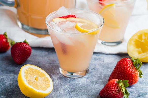 cold glasses of keto strawberry lemonade on the counter with lemons and strawberries laid around