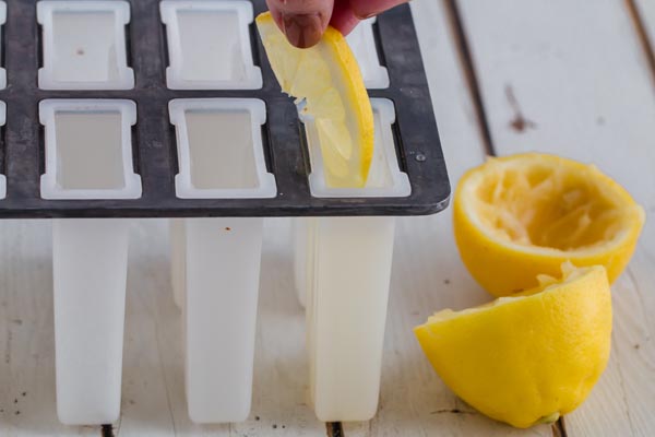 adding pink lemonade and lemon slices to a popsicle mold