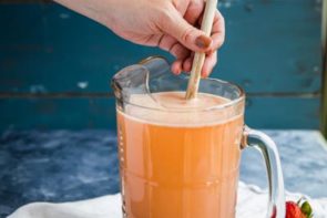 stirring a pitcher of strawberry lemonade with a wooden spoon