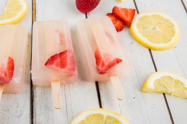 wooden sticks inside pink lemonade popsicles with strawberries nearby