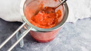 straining strawberries in a metal sieve with a pyrex measuring cup underneath