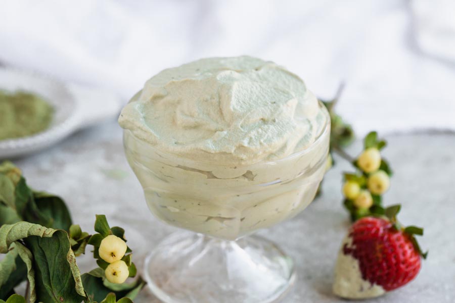 fluffy green whipped cream in a clear dish next to a strawberry
