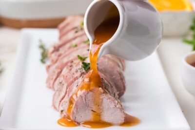 Sweet citrus glaze being poured over sliced pork tenderloin on a serving platter.