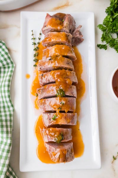 Overhead view of sliced pork tenderloin covered in glossy orange citrus glaze on a white serving platter.