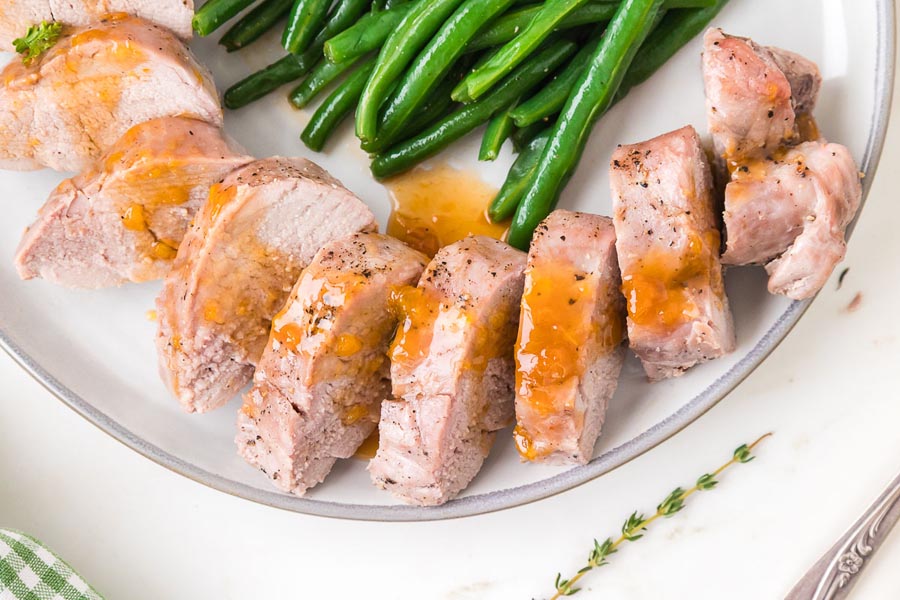 Close-up of juicy pork tenderloin slices drizzled with sweet citrus glaze and plated with green beans.